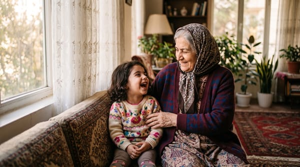 A grandmother and her young granddaughter laughing together on a sofa in warm afternoon light